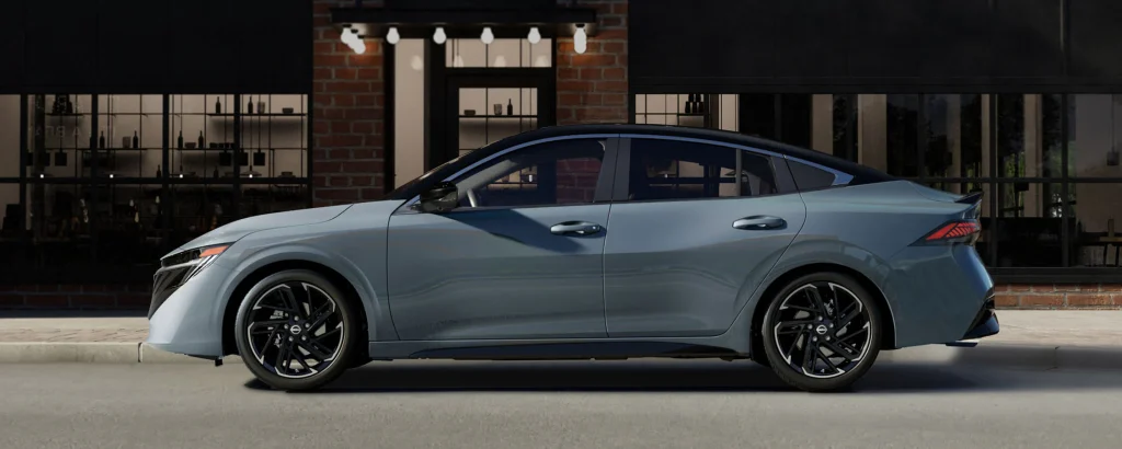 A side view of a sleek gray Nissan Sentra parked in front of a modern building with large windows.