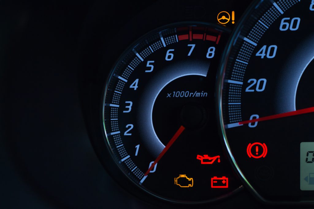 A close-up of a car's digital dashboard at night, showing the tachometer and several illuminated warning lights, including engine, battery, and oil pressure.