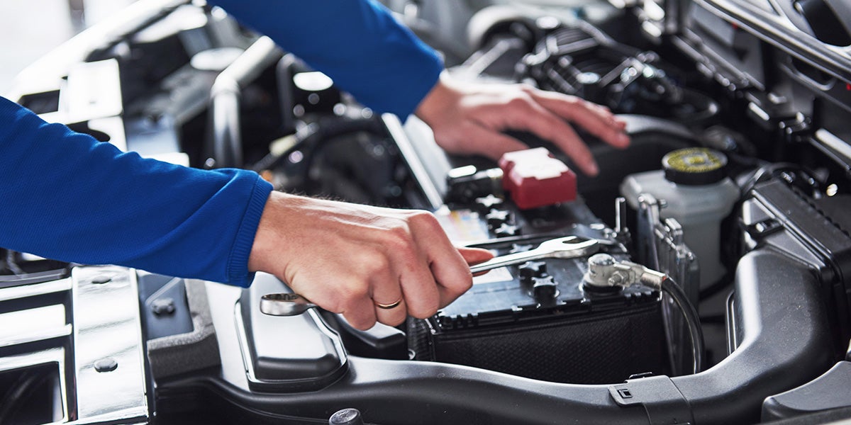 A technician using a wrench to service a car battery under an open hood.